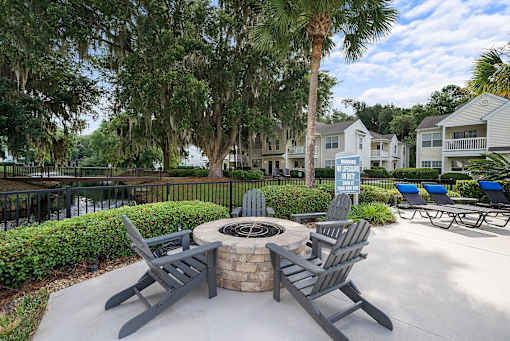 A fire pit surrounded by chairs in a sunny outdoor setting.