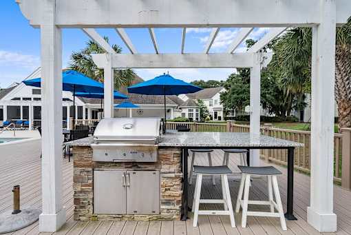 A white pergola with a grill and two chairs under it.