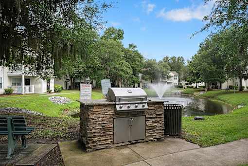 A BBQ grill is in the middle of a grassy area with a sign in front of it.
