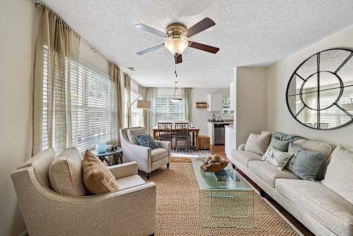A living room with a beige couch, a glass coffee table, and a ceiling fan.