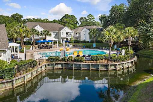 A pool surrounded by a fence and trees with houses in the background.
