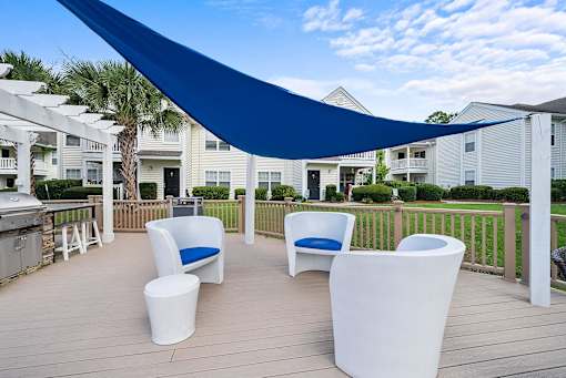A blue shade sail over a white patio furniture set.