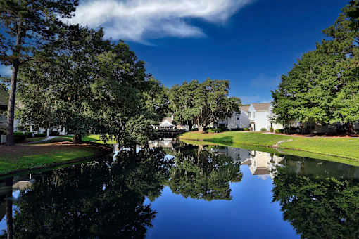 A serene landscape with a pond, trees, and a white building in the distance.