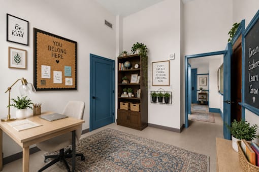 A room with a cork board on the wall that says "You belong here" and a desk with a laptop and a plant.