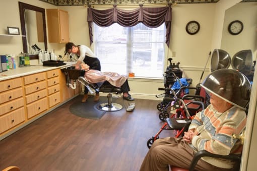 a patient sits in a chair while a woman cuts his hair in a patient room