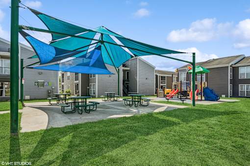 A playground with a blue umbrella and picnic tables.