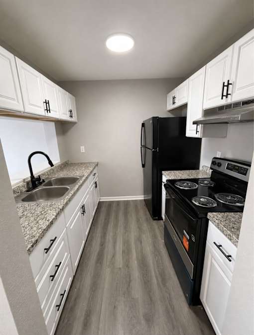 A black refrigerator sits in a kitchen with white cabinets and a granite countertop.