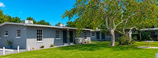 A grey house with a tree in front.