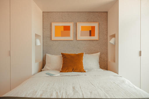 a small bedroom with a bed and two orange paintings on the wall at Scout Living, powered by Placemakr Apartments, Atlanta