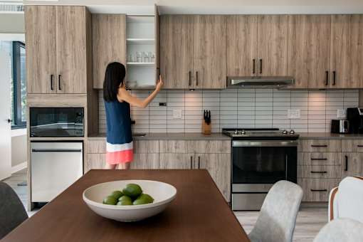 A woman is opening a cabinet in a modern kitchen at Coda on Half Apartments, Washington