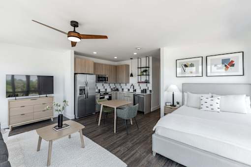 A modern bedroom with a bed, a table, a ceiling fan, and a kitchen area in the background at Anthem House Apartment , Huntsville, Alabama