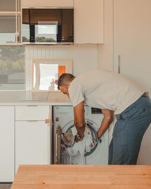 a man is loading a washer into a washing machine in a kitchen at Scout Living, powered by Placemakr Apartments, Atlanta, GA, 30308