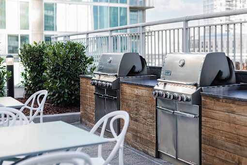 Two grills are on a patio with tables and chairs.