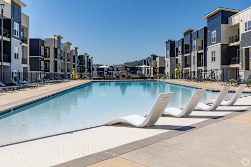 A swimming pool surrounded by sun loungers and apartment buildings.