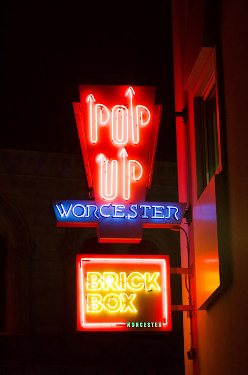 A neon sign for a place called "Brick Box" is lit up at night.