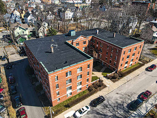 Two red brick buildings with green roofs and parking lots in front.