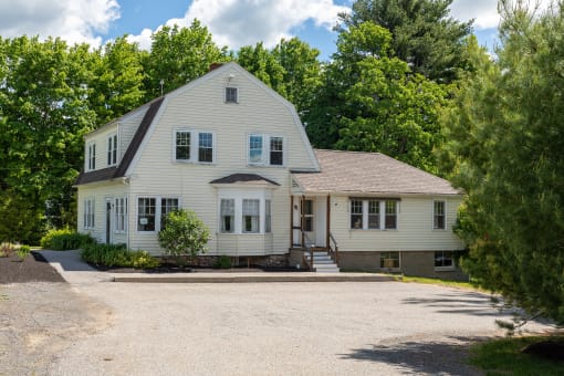 a large white house with a gravel driveway and trees in the background