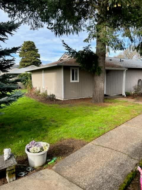 A house with a brown roof and a grey siding is surrounded by a green lawn and trees.
