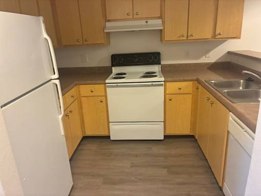A kitchen with a white refrigerator, white stove, and wooden cabinets.