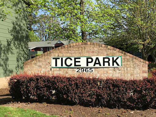 A sign that says Tice Park stands in front of a green building.