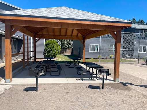 A wooden pavilion with a table and chairs is set up in a sandy area.