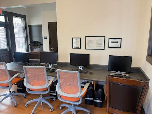 A room with a desk, chairs and computer monitors.