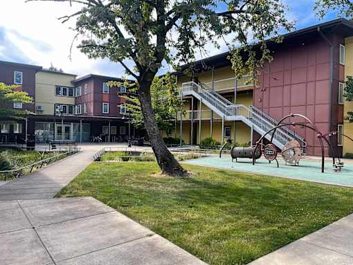 A tree stands in front of a building with a red wall and a staircase.