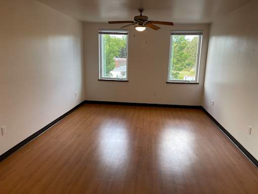 A room with a ceiling fan and two windows.