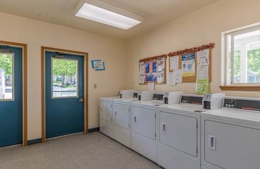 A laundromat with washers and dryers and a bulletin board.