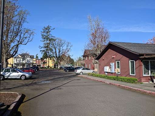 A street view with cars parked on the side of the road and a red building in the background.