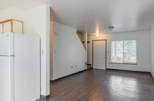 A white refrigerator stands in a room with wood floors and white walls.