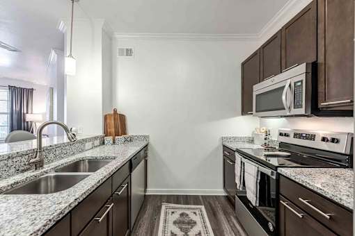 A kitchen with dark brown cabinets and granite countertops at 95twenty Apartments, Austin, 78717