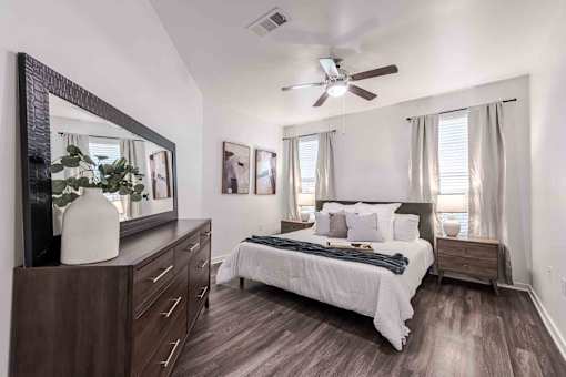 A bedroom with a bed, dresser, mirror, and a ceiling fan at 95twenty Apartments, Texas