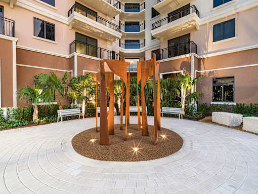 A large sculpture in the middle of a courtyard surrounded by benches and plants.