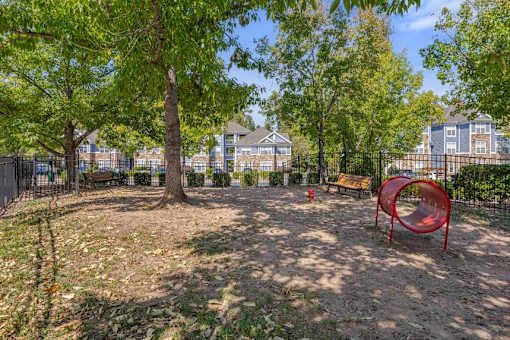 A playground with a red slide and a tree in the middle of a dirt area.