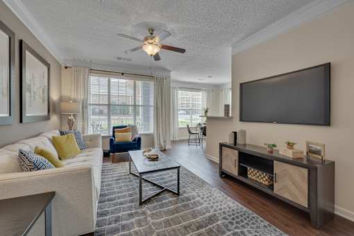A living room with a white couch, a coffee table, and a flat screen TV mounted on the wall.