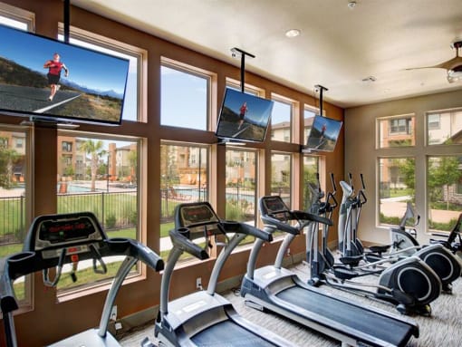 a gym with a lot of treadmills and televisions