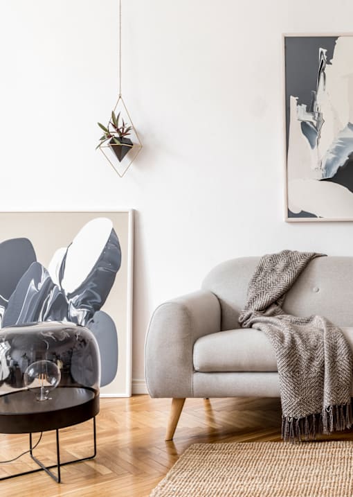 A grey couch with a blanket on it sits in front of a wall with a black and white abstract painting.