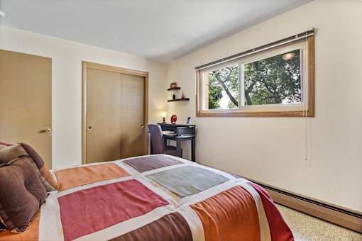 A bedroom with a bed, desk, and window.