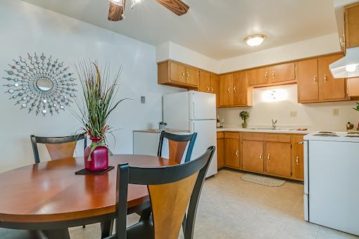 A kitchen with a table and chairs in the foreground and a white refrigerator in the background.