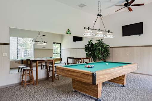 A pool table is in the middle of a room with a ceiling fan and a television mounted on the wall.