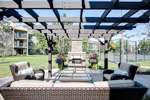 A patio with a wicker sofa and a table with a vase of flowers on it.