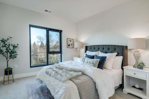 A bedroom with a large bed, a nightstand, and a window with a view of trees.