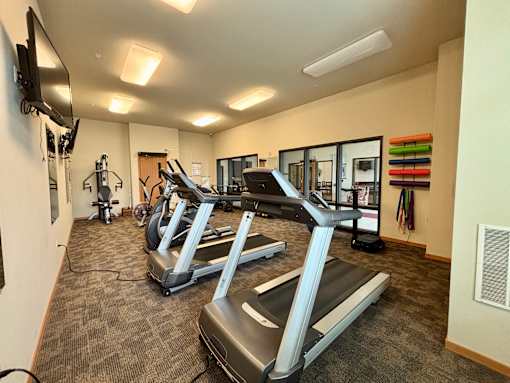 A gym with treadmills and a television mounted on the wall.