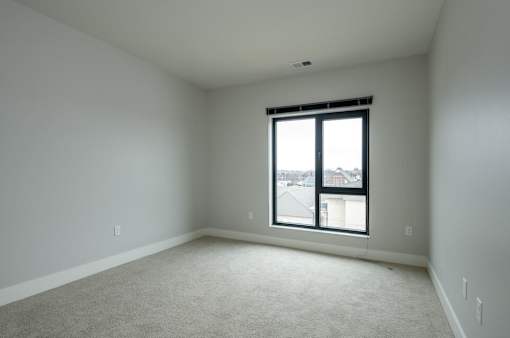 A room with a carpeted floor and a window showing a view of buildings outside.