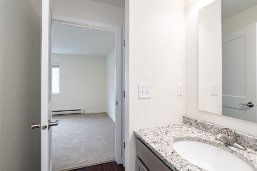 a bathroom with a sink and a mirror and an open door to a bedroom