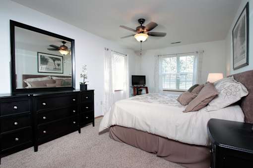 A bedroom with a large bed, a dresser, and a ceiling fan.