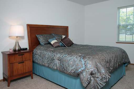 A bed with a wooden headboard and a blue comforter with a pattern on it.