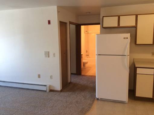 A white refrigerator in a kitchen with a carpet on the floor.