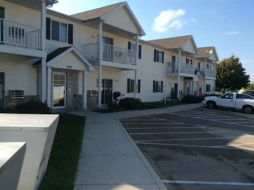 A white car is parked in a parking lot in front of apartment buildings.